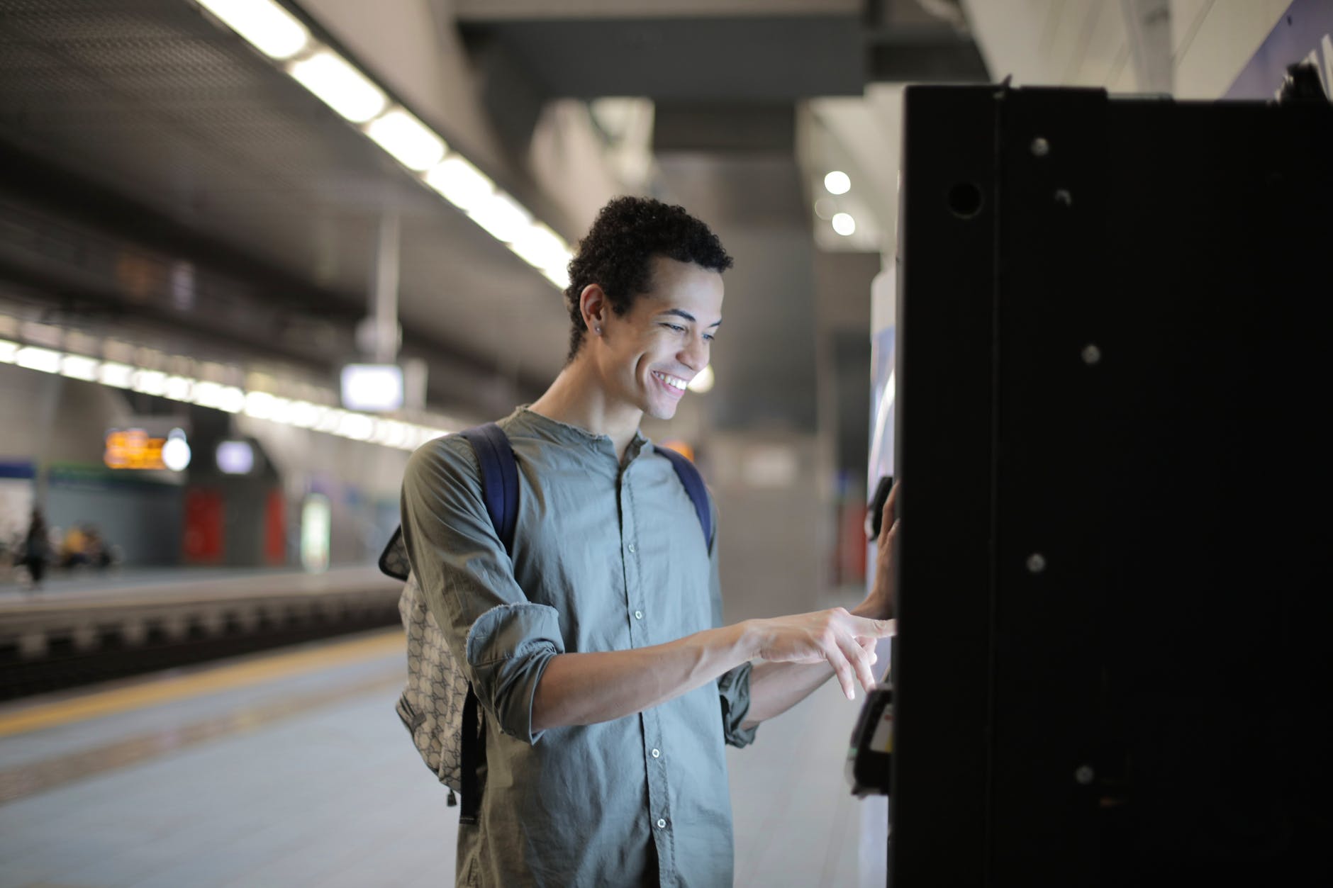 cheerful ethnic man using ticketing machine at subway station