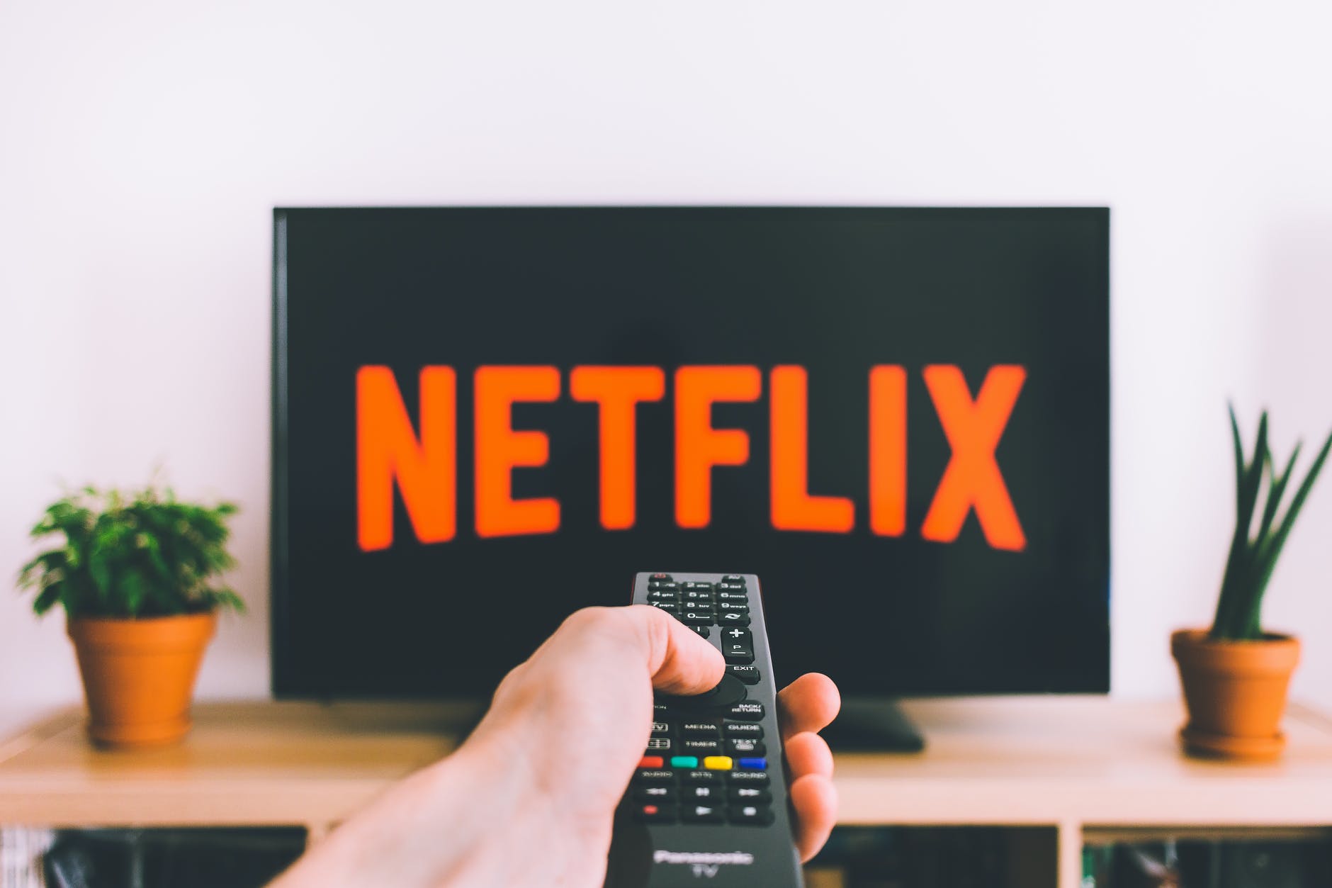 closeup photo of person holding panasonic remote control in front of turned on smart television